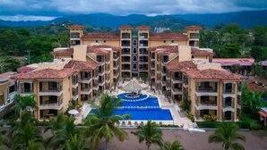 A multi-story hotel with a central swimming pool, surrounded by palm trees and a mountainous backdrop. - Bahia Encantada G5 (Jacó)