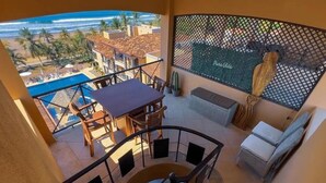 A balcony with a table and chairs, a cushioned seating area, and a view of the beach and ocean. - Bahia Encantada G5 (Jacó)