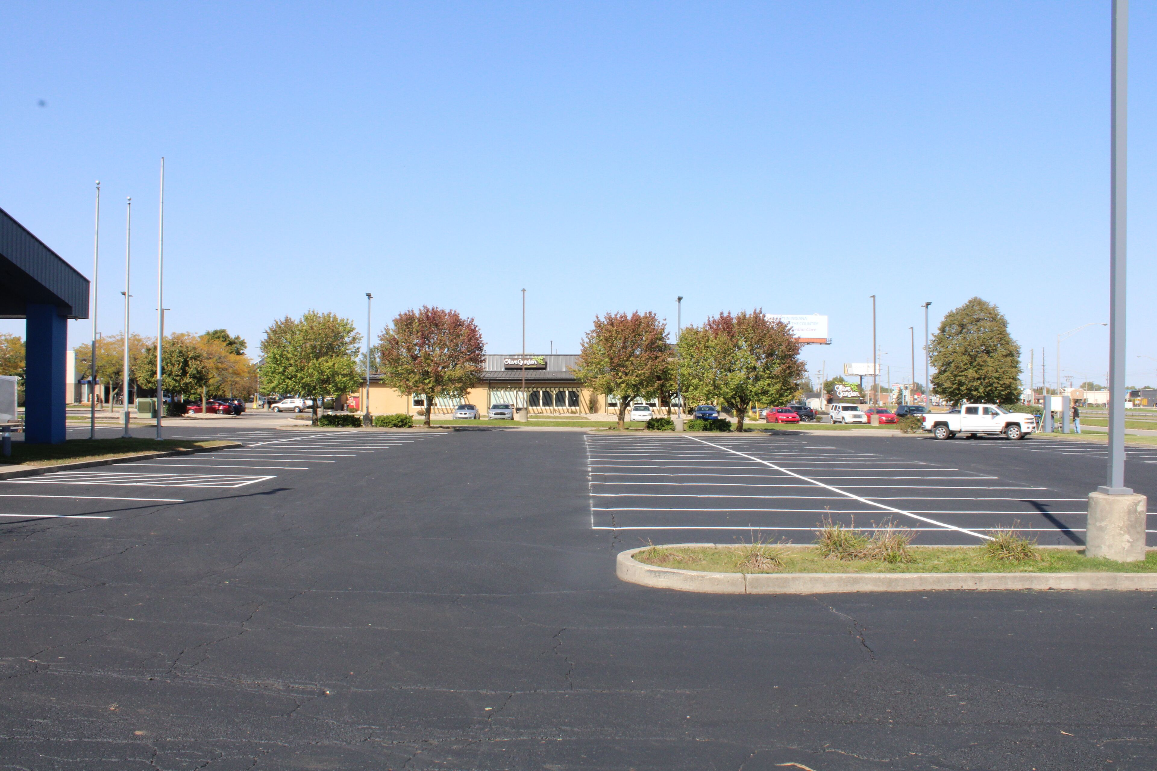 Un parking avec des places délimitées, un bâtiment avec une enseigne et des arbres aux feuilles d’automne.