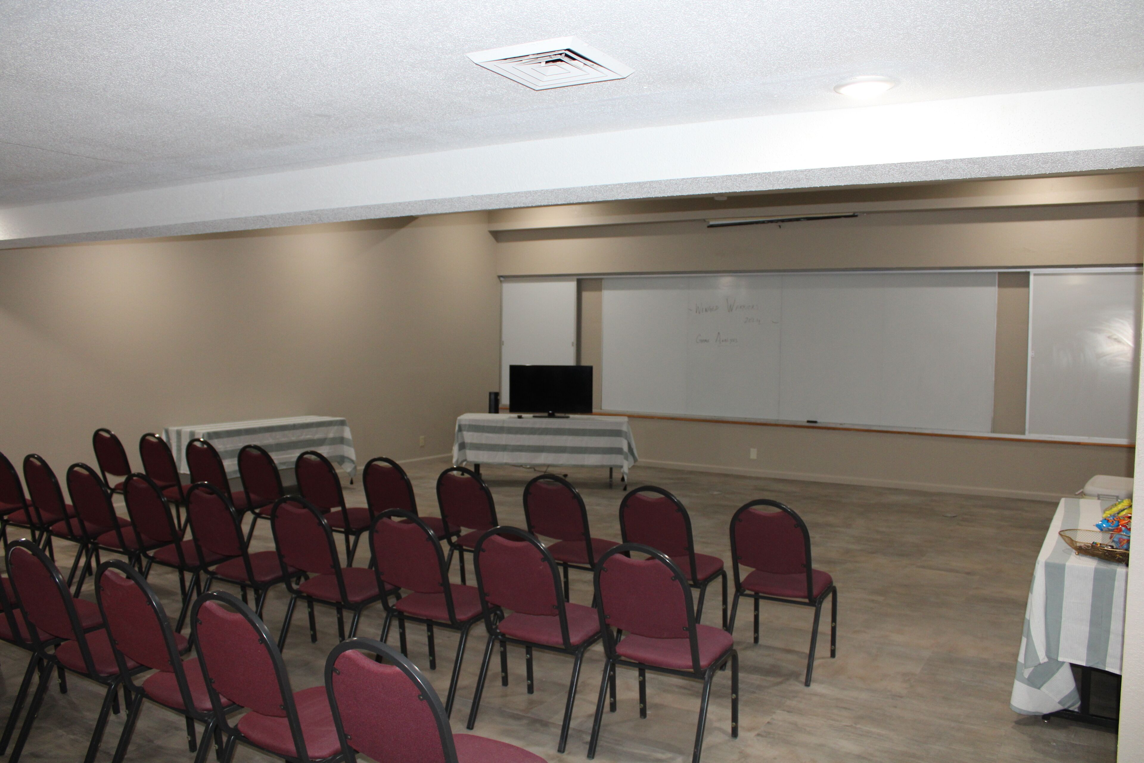 A conference room with rows of chairs, a whiteboard, a projector, and a table with a striped tablecloth.