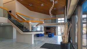 Un hall d’entrée spacieux avec un escalier en colimaçon, une grande plante en pot et un coin salon avec des canapés bleus.