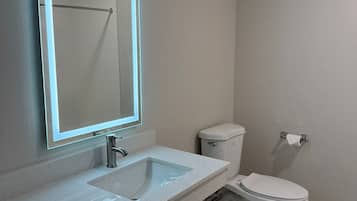 A modern bathroom with a large mirror, a sink, and a toilet.