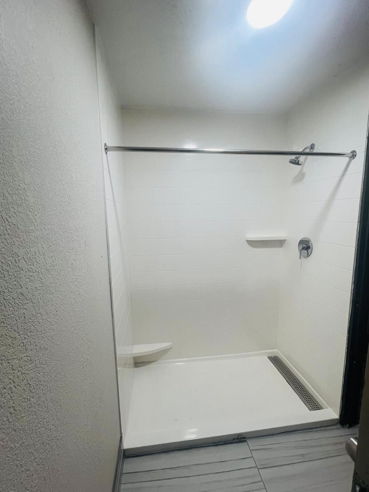 A small, enclosed shower area with a glass door, a metal showerhead, and a white tiled floor.
