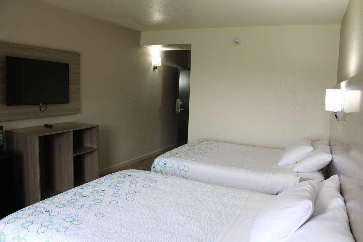 A hotel room with two beds, a TV mounted on the wall, and a wooden cabinet.
