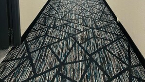 Un couloir d’hôtel avec un tapis à motifs, des portes des deux côtés et des panneaux indiquant les sorties de secours.