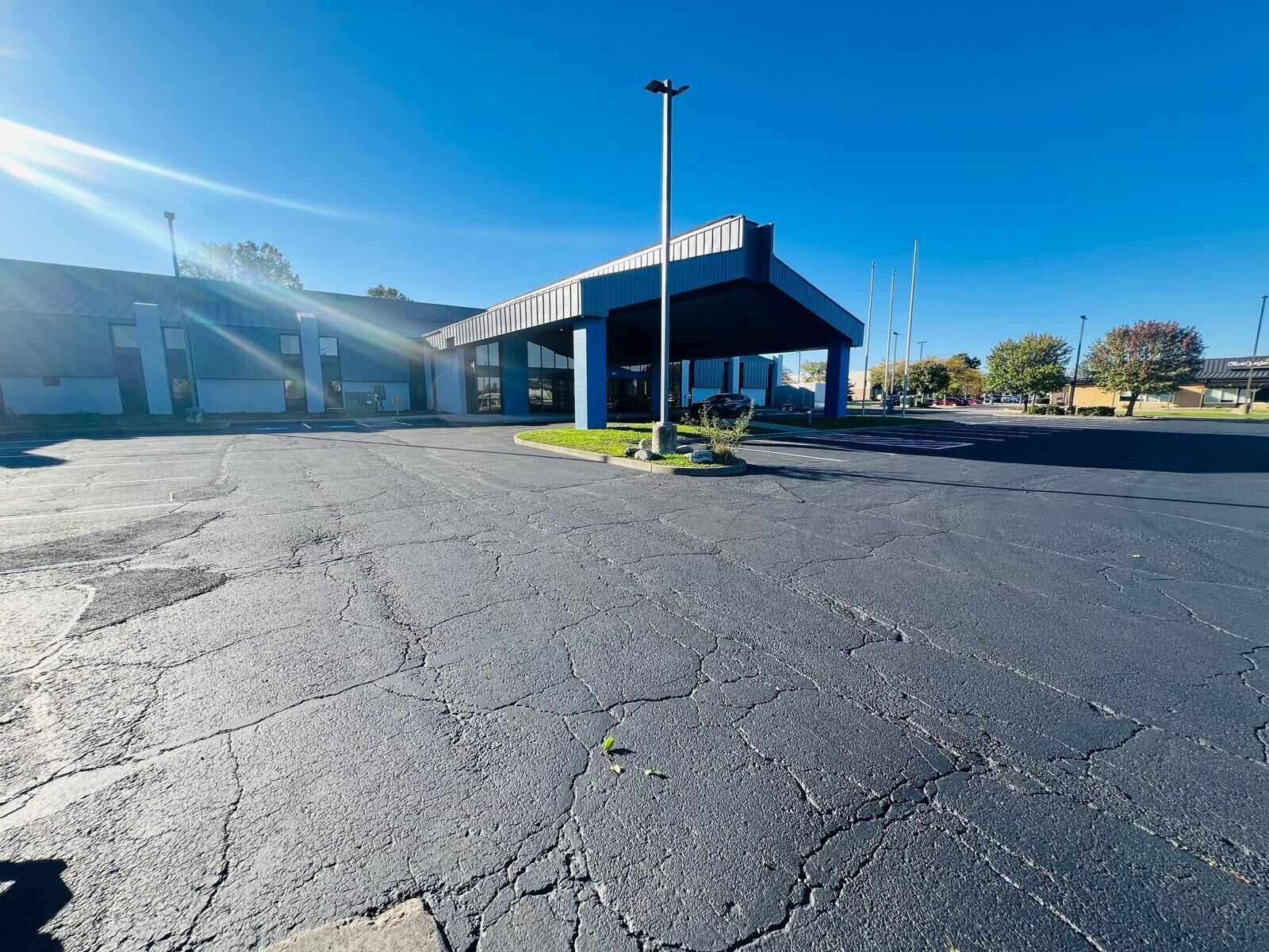 A parking lot with a building featuring a covered area and a clear blue sky.