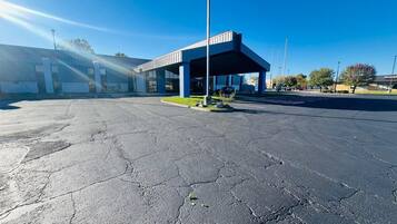 A parking lot with a building featuring a covered area and a clear blue sky.