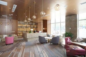 Un lobby moderno de hotel con zona de bar, arreglos de asientos y ventanas amplias.