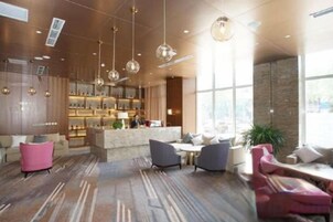 Un lobby moderno de hotel con zona de bar, arreglos de asientos y ventanas amplias.
