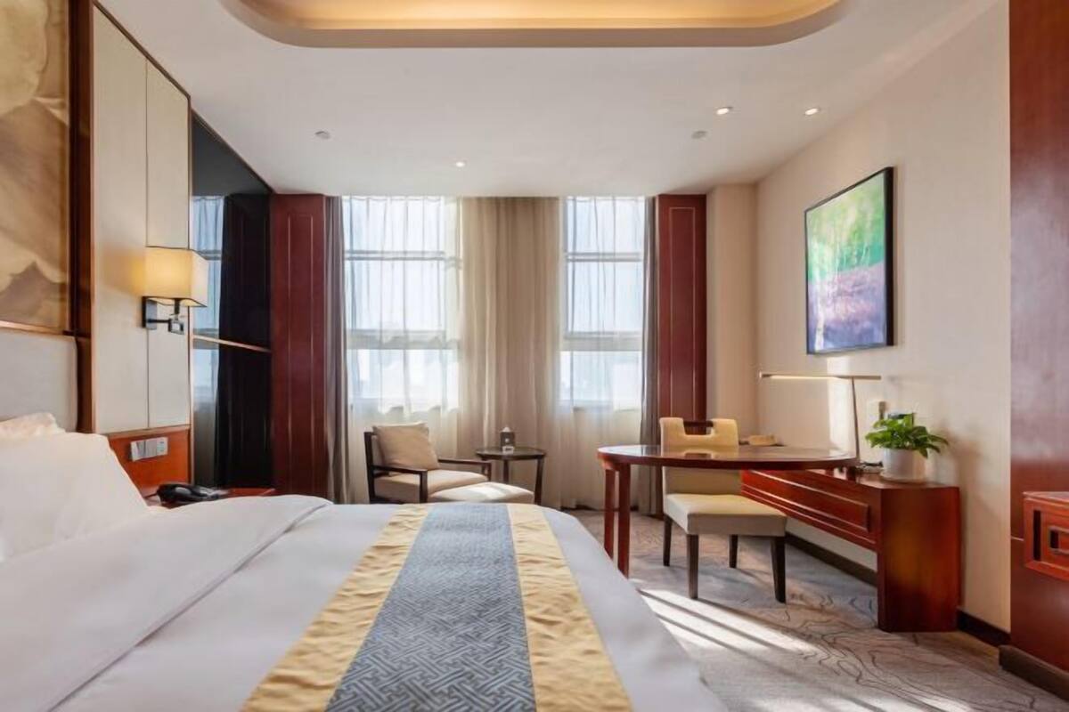 Een hotelkamer met een groot bed, een bureau, een stoel, een klein tafeltje en een schilderij aan de muur.