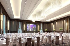 Un salón de banquetes con mesas redondas, sillas y una pantalla grande.