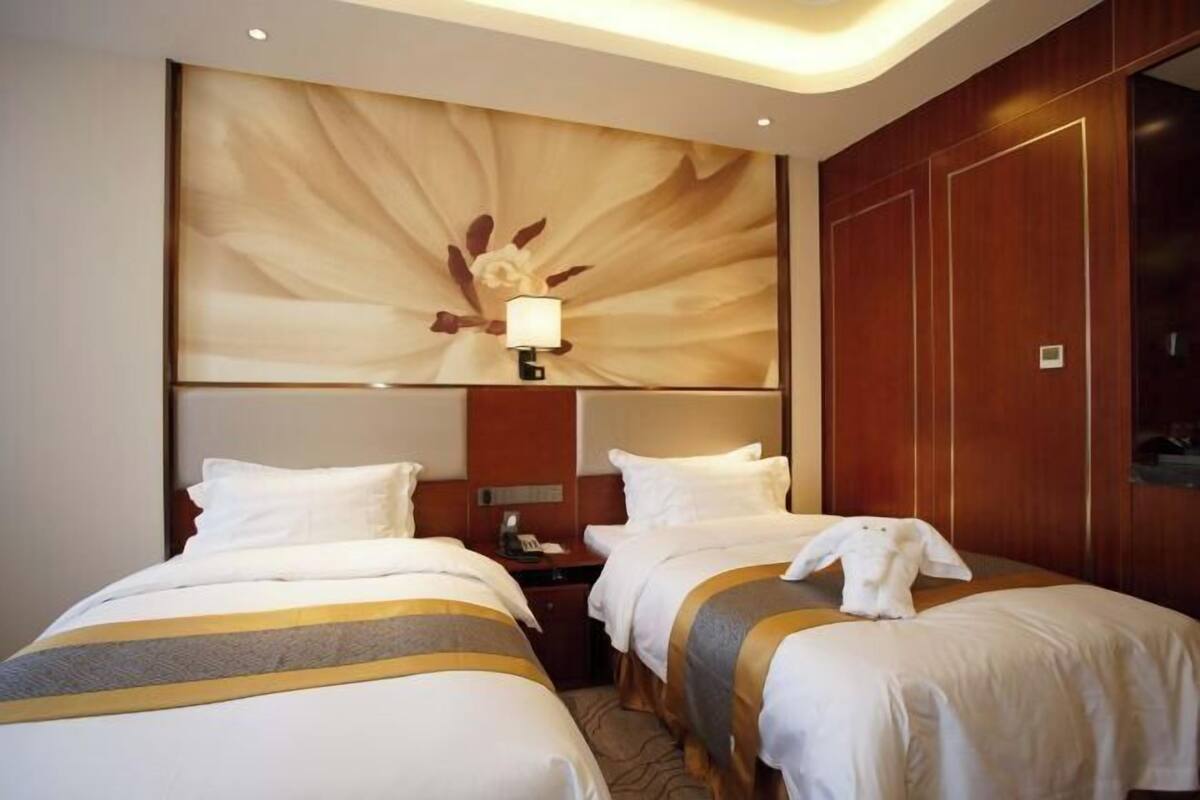Een hotelkamer met twee bedden, een wandlamp, een nachtkastje en een houten garderobe.