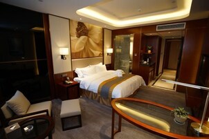 Una habitación de hotel con una cama grande, un escritorio, una silla, una mesita y un espejo.