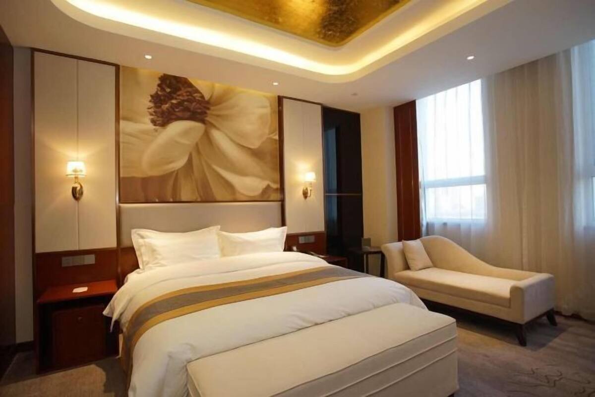 Een hotelkamer met een groot bed, een bank, een kunstwerk aan de muur en een plafondlamp.