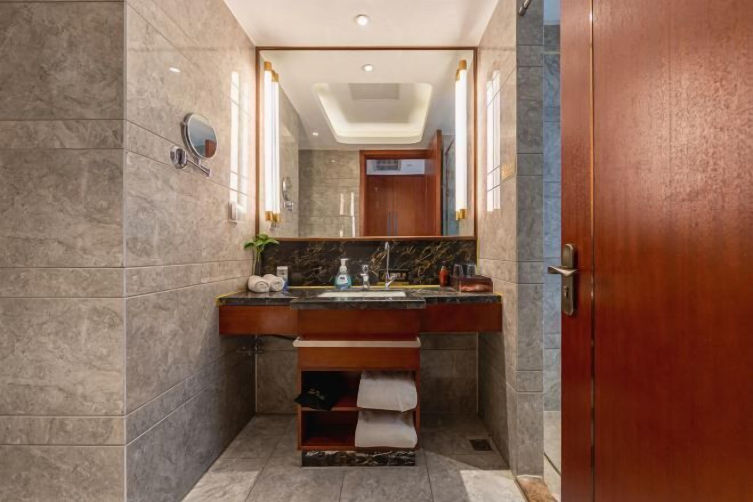 A bathroom with a marble wall, a wooden vanity, a mirror, and a towel rack.