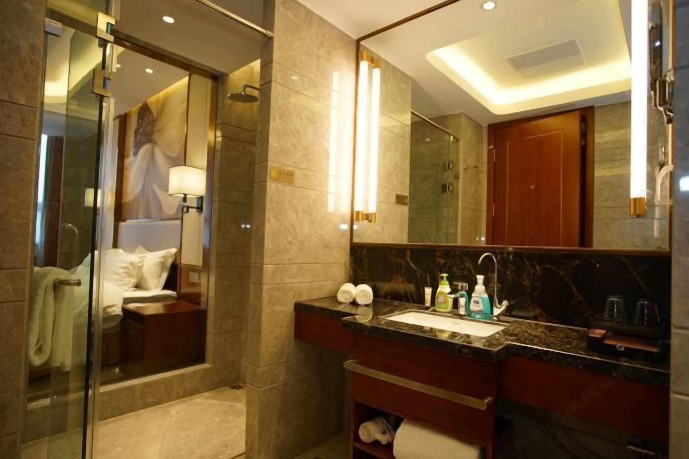 A modern bathroom with a glass shower enclosure, a large mirror, and a marble countertop.