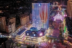 A high-rise building with a prominent vertical light display, surrounded by other buildings and a busy street. - Qingdao Haina Baichuan Hotel (Pingdu)