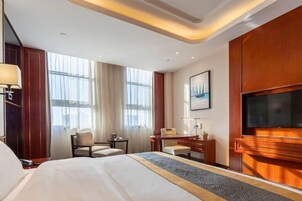 Una habitación de hotel con una cama grande, un escritorio, una silla, un televisor y una ventana con cortinas.