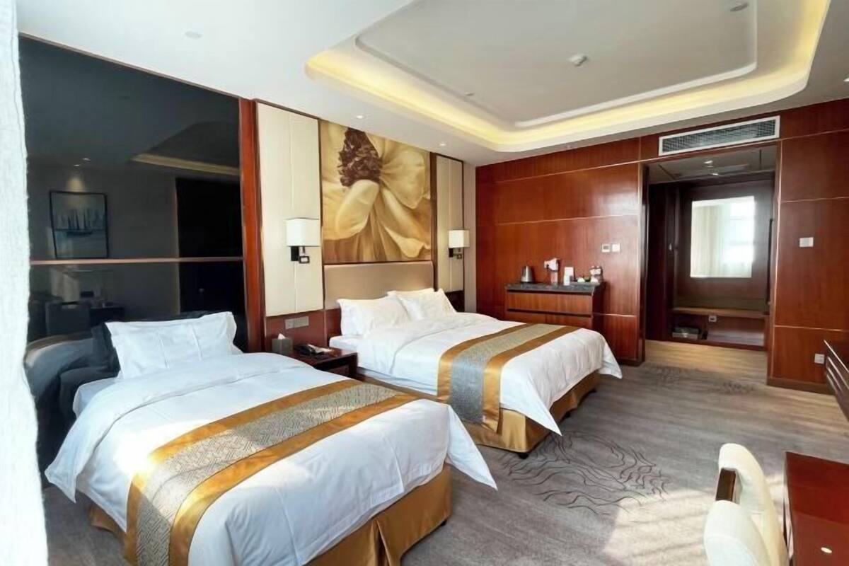 Een hotelkamer met twee bedden, een bureau, een grote spiegel en een schilderij aan de muur.