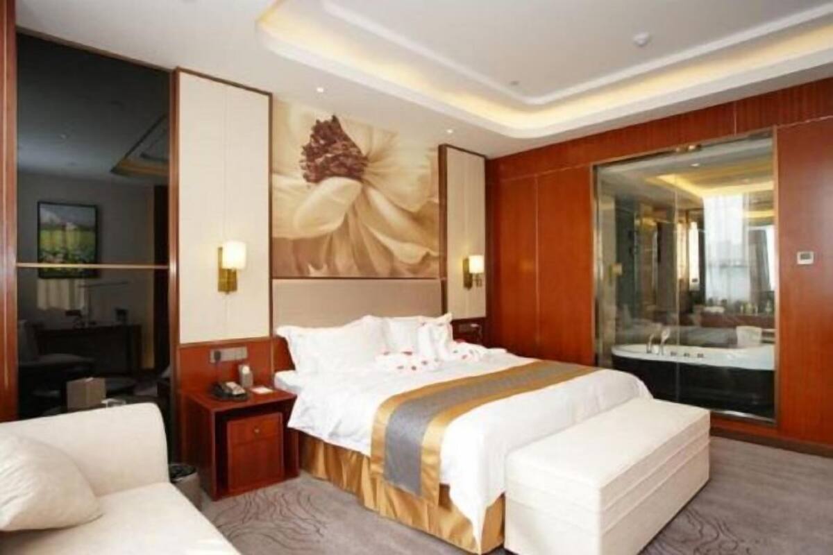 Een hotelkamer met een groot bed, een nachtkastje, een spiegel en uitzicht op een wellnessruimte.
