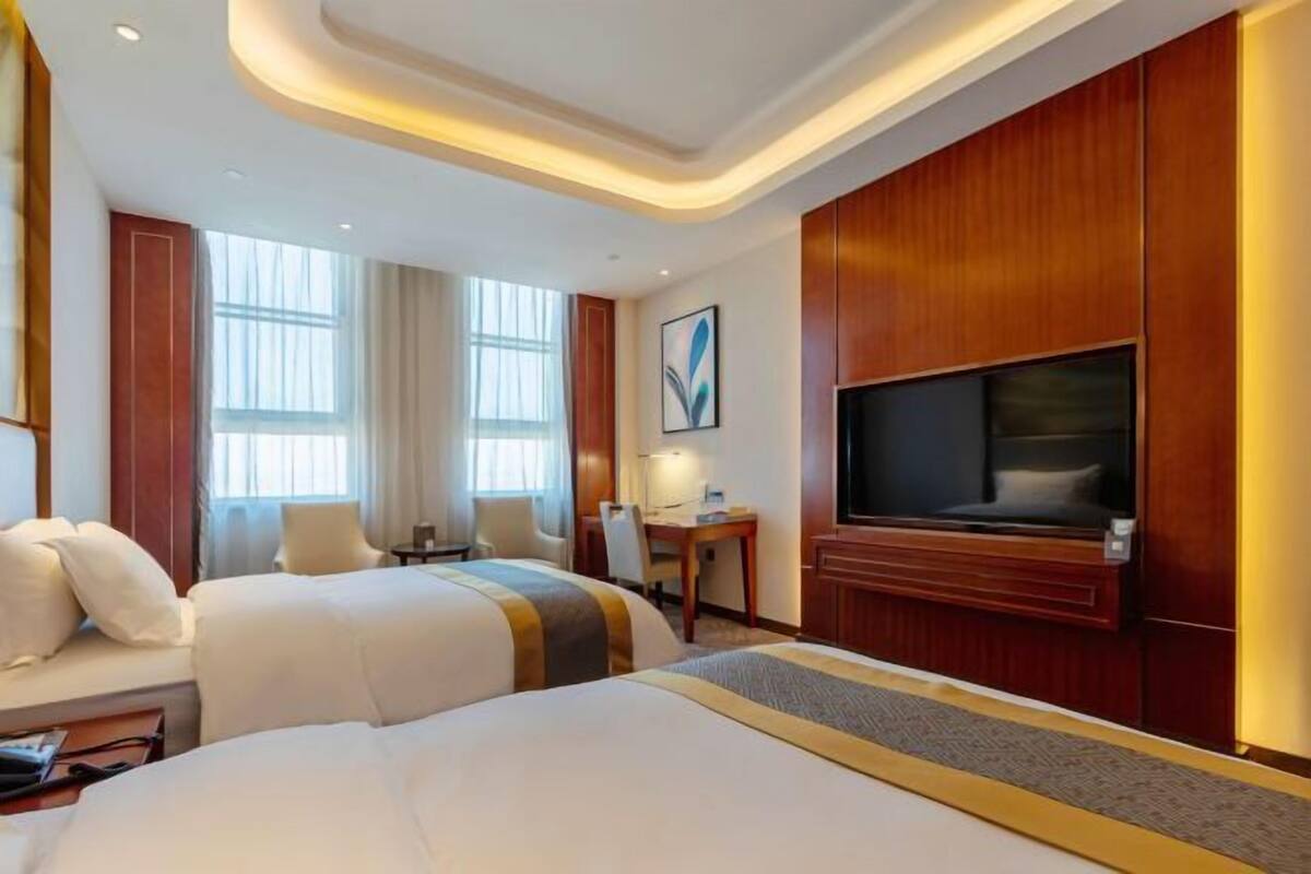 Een hotelkamer met twee bedden, een bureau, een stoel, een televisie en een raam.