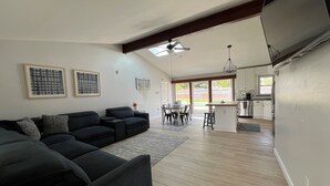 Een moderne woonkamer met een modulaire bank, een eethoek met een tafel en stoelen, en een keuken met een koelkast en kasten.