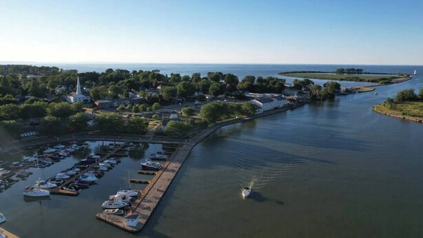 An aerial view of a marina with boats docked, a church, and a lighthouse in the distance.