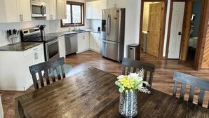 A modern kitchen with white cabinets, stainless steel appliances, and a wooden dining table with chairs.