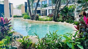 A pool surrounded by lush greenery and a multi-story building with balconies. - Tulum Stylish 2BR Penthouse W/private Terrace, Grill & Pool (Tulum)