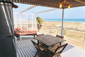 Un espace extérieur abrité, équipé d’une table et de chaises, d’un fauteuil de relaxation et offrant une vue sur la plage.