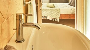 Ein Badezimmer mit einer großen Badewanne, Holzschränken und einem sichtbaren Schlafzimmer mit Bett und Vorhängen.