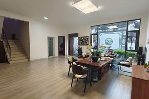 Een ruime woonkamer met houten vloer, een eettafel met stoelen, een trap en grote ramen met uitzicht.