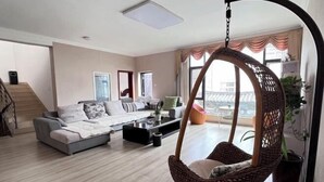 Un salon moderne avec un canapé gris, un fauteuil suspendu et une grande fenêtre donnant sur un beau paysage.