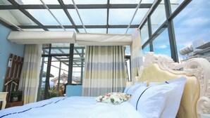 Une chambre avec un lit, des rideaux et une vue dégagée sur l’extérieur grâce à de grandes fenêtres.