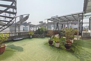 Een dakterras met kunstgras, plantenbakken en een pergola.