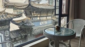 Un balcon agrémenté d’une maquette d’architecture chinoise traditionnelle, de fauteuils en osier et d’une table en verre.