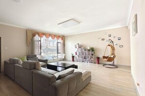 A living room with a sectional sofa, a coffee table, and a hanging chair. There is a window with curtains, a bookshelf, and a potted plant. - Zuimei Dali Boutique Inn (Dali City)