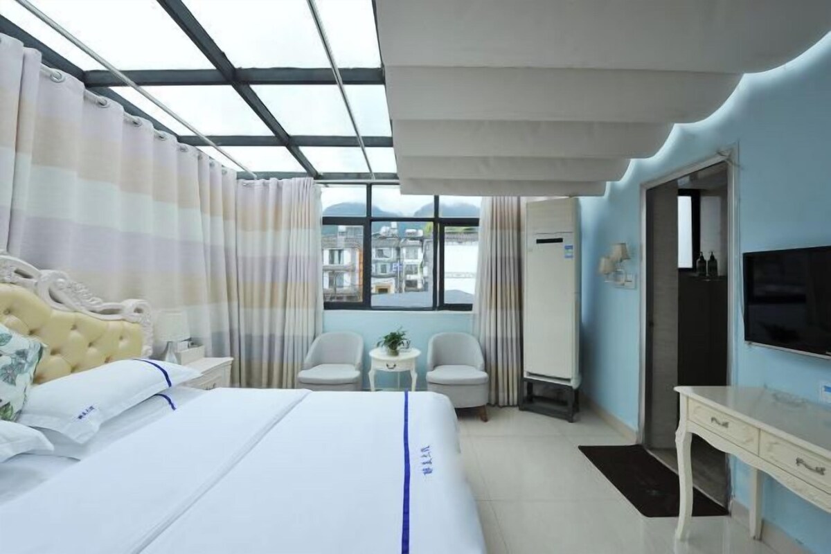 A hotel room with a bed, two chairs, a small table, a TV, and a window with curtains.