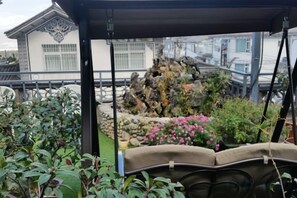 Un'area salotto esterna coperta con vista su un giardino e un edificio sullo sfondo.