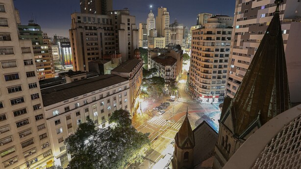 Un paisaje urbano nocturno con rascacielos, una calle con semáforos y una imponente aguja de iglesia.