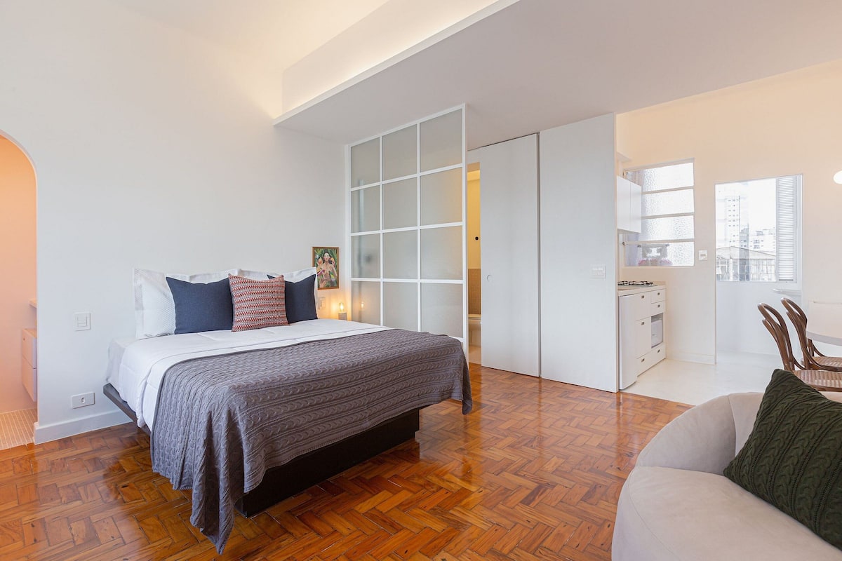 A bedroom with a bed, a sofa, a kitchen area, and a sliding door closet.