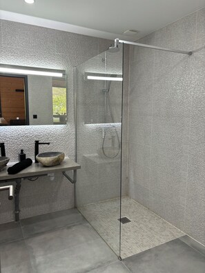 A modern bathroom with a glass-enclosed shower, a stone sink, and a large mirror.