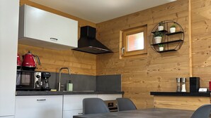 A modern kitchen with wooden paneling, a black range hood, a red kettle, and a round shelf with potted plants.
