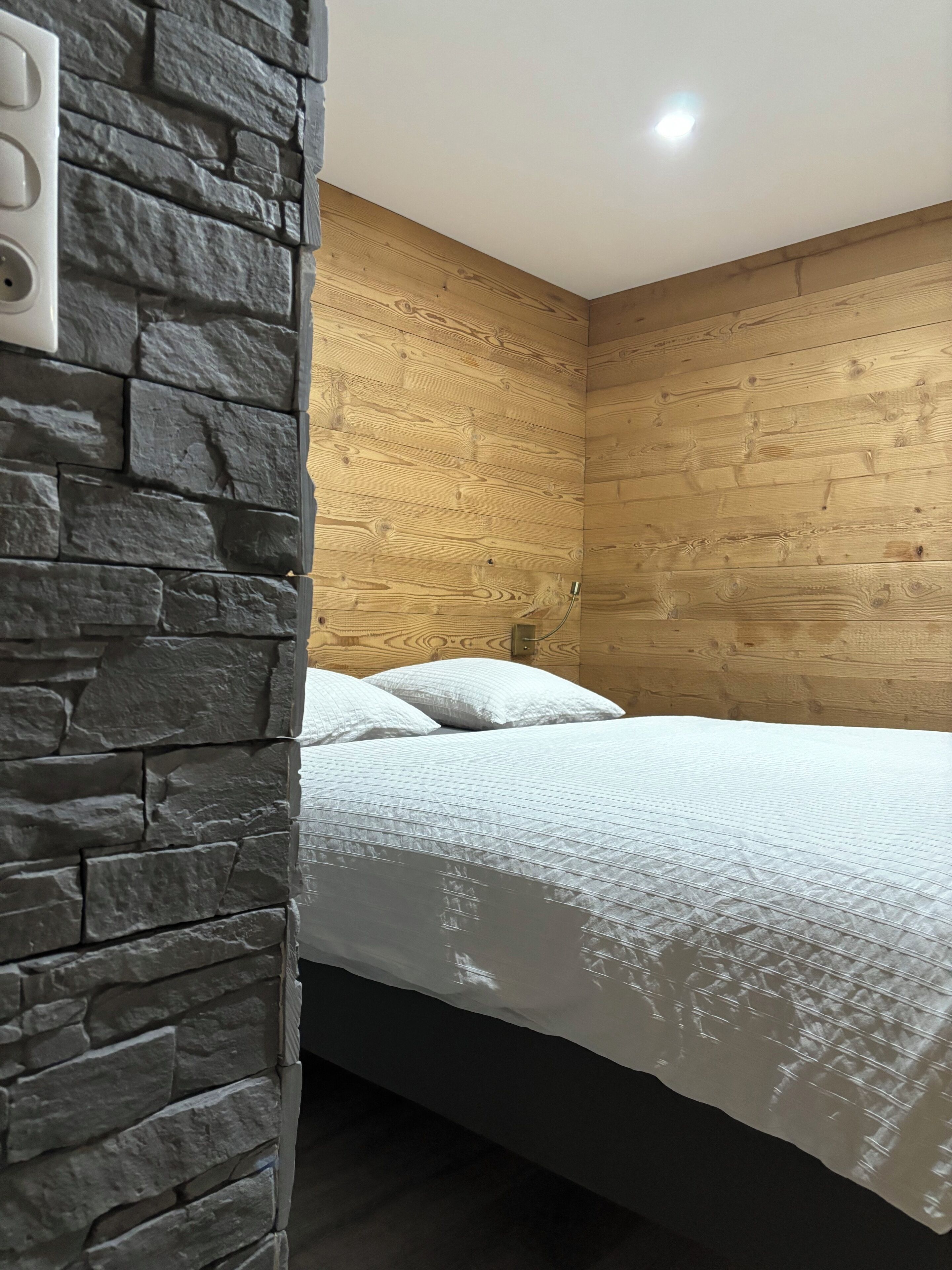 Une pièce avec un lit adossé à un mur en pierre et un lambris en bois.