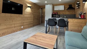 A modern kitchen with wooden walls, a dining area with a table and chairs, and a living area with a sofa.