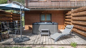 A wooden cabin with a balcony, outdoor seating, and a hot tub.