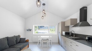 A modern kitchen with white cabinets, a black range hood, and a window with a view of greenery. - Chalet du Petit-Bouchot : cosy, private spa, 2p (Rochesson)