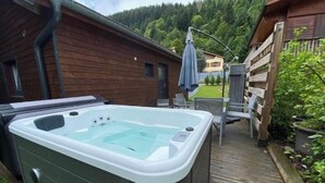 A hot tub on a wooden deck with a view of a forested hillside. - Chalet du Petit-Bouchot : cosy, private spa, 2p (Rochesson)