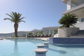 A pool area with lounge chairs, palm trees, and a view of mountains.