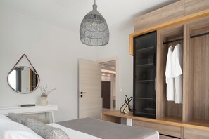 A bedroom with a bed, bedside table, mirror, hanging light fixture, wardrobe, and a door leading to another room.